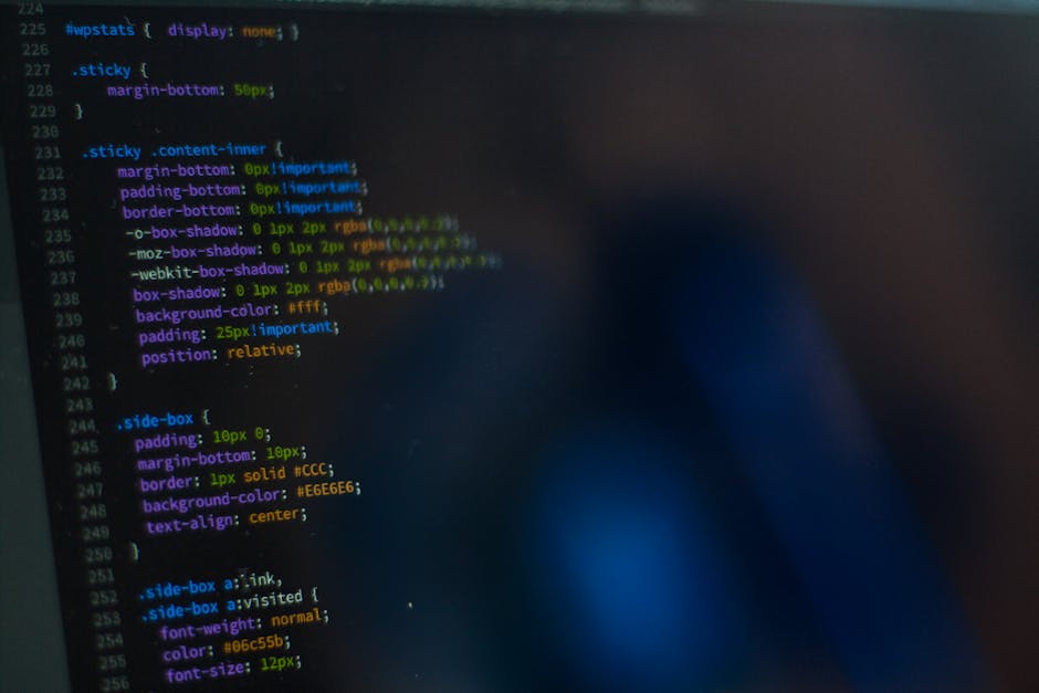 A close-up view of a computer screen displaying lines of colorful programming code, primarily in shades of blue, green, yellow, and purple, on a dark background. The code includes CSS styling elements